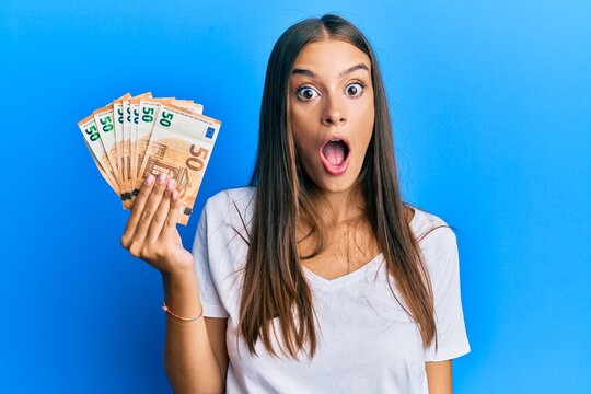 Young hispanic woman holding 50 euro banknotes scared and amazed with open mouth for surprise, disbelief face
