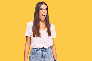 Young hispanic woman wearing casual white tshirt angry and mad screaming frustrated and furious, shouting with anger. rage and aggressive concept.