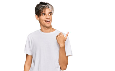 Young hispanic man wearing casual white tshirt smiling with happy face looking and pointing to the side with thumb up.