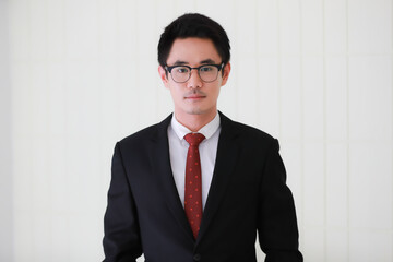 Portrait of young and cute Asian man wearing black suit and eyeglasses pose to camera with self-confidence and friendly face