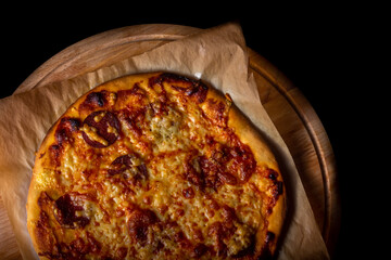 Hot pizza on baking paper on wooden plate