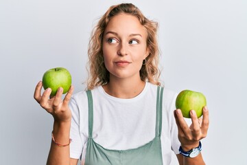 Beautiful caucasian woman holding green apples smiling looking to the side and staring away thinking.
