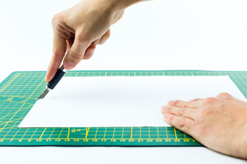 hand cutting a sheet of paper with a utility knife on white background