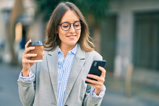 Young hispanic businesswoman using smartphone and drinking take away coffee at the city.