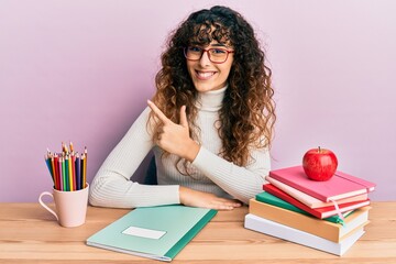 Young hispanic girl studying for school exam smiling cheerful pointing with hand and finger up to the side