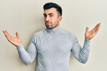 Young hispanic man wearing casual clothes clueless and confused with open arms, no idea and doubtful face.