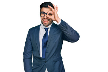 Hispanic man with beard wearing business suit and tie smiling happy doing ok sign with hand on eye looking through fingers