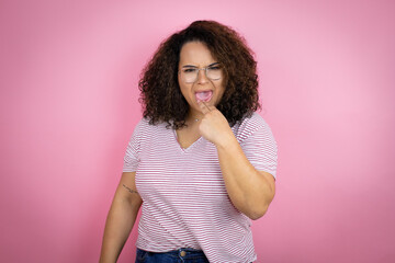 Young african american woman wearing red stripes t-shirt over pink background disgusted with her hand inside her mouth