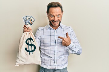 Middle age man wearing business shirt holding dollars bag pointing finger to one self smiling happy...