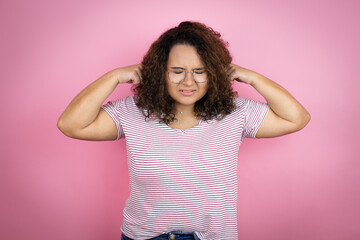 Young african american woman wearing red stripes t-shirt over pink background covering ears with fingers with annoyed expression for the noise of loud music. Deaf concept.