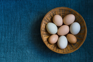 Organic chicken eggs in wicker basket on blue textile background with copy space