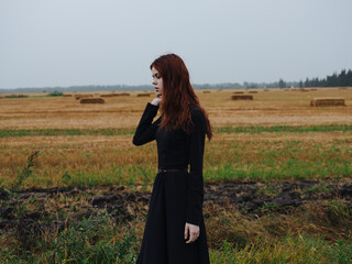 A beautiful woman in a black dress walks in a field on nature in autumn