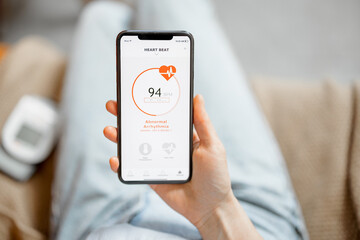 Woman showing a heart rate on smartphone while sitting on sofa at home. Health and wellness concept. Focus on phone screen. Close up