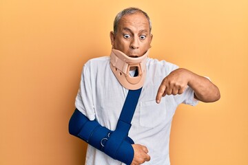 Handsome mature senior man wearing cervical collar and arm on sling pointing down with fingers...
