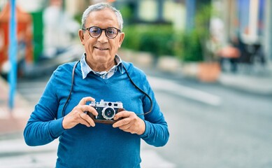 Senior grey-haired tourist man smiling happy using vintage camera at the city.