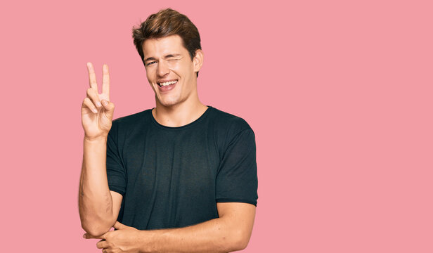Handsome caucasian man wearing casual clothes smiling with happy face winking at the camera doing victory sign. number two.