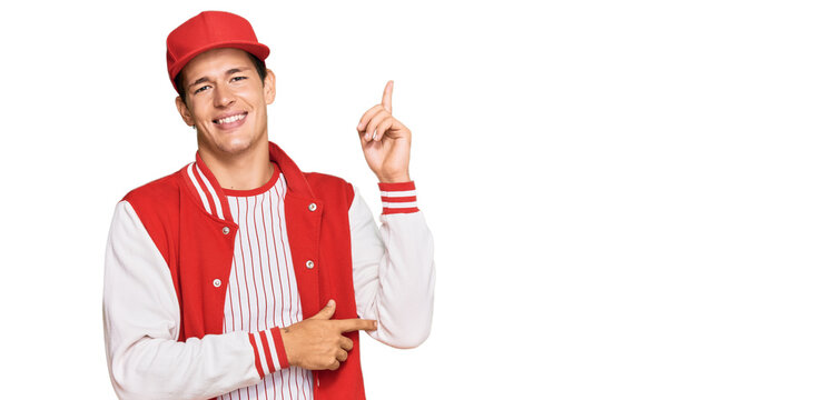 Handsome caucasian man wearing baseball uniform with a big smile on face, pointing with hand and finger to the side looking at the camera.