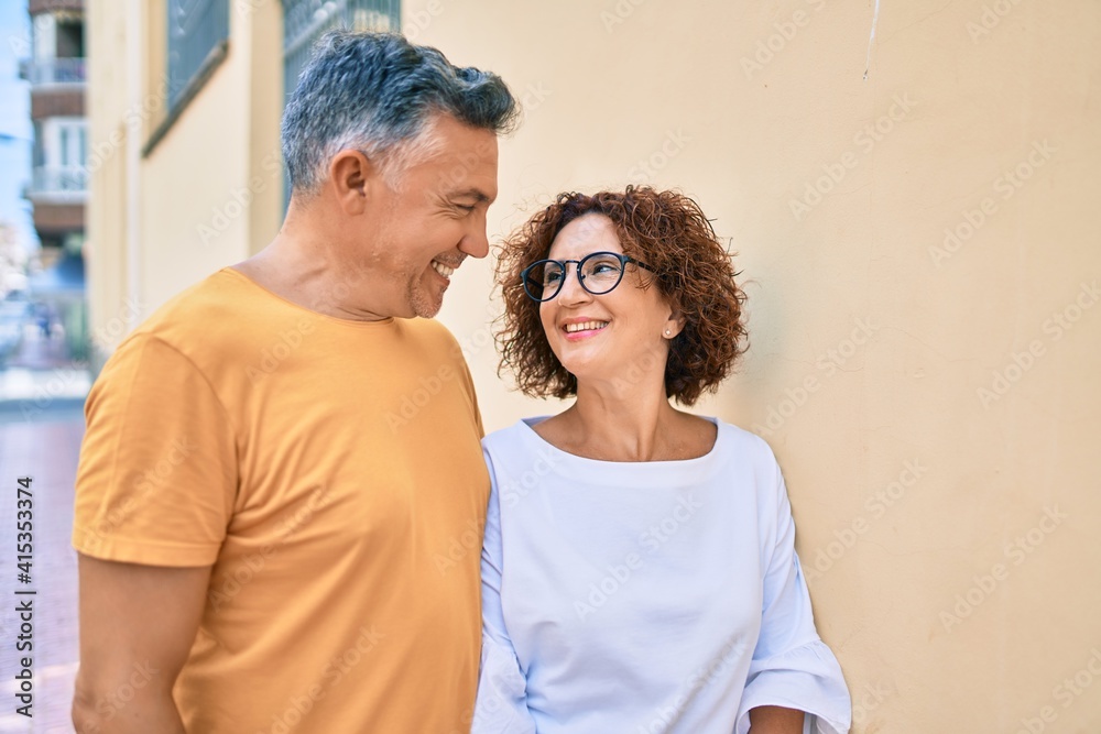 Poster middle age couple smiling happy leaning on the wall at street of city.