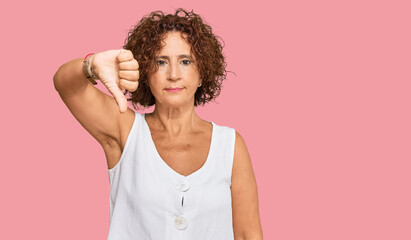 Beautiful middle age mature woman wearing casual white shirt looking unhappy and angry showing rejection and negative with thumbs down gesture. bad expression.