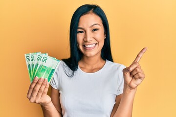 Beautiful hispanic woman holding 50 norwegian krone banknotes smiling happy pointing with hand and...