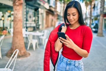 Young latin woman smiling happy using smartphone at the city.