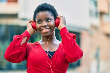 Young african american woman smiling happy listening to music using headphones at the city.