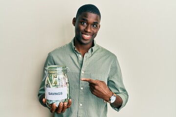 Young african american man holding jar with savings smiling happy pointing with hand and finger