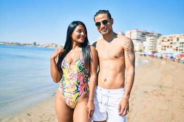 Young latin couple wearing swimwear  smiling happy and hugging at the beach.