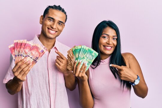 Young Latin Couple Holding South African Rand Banknotes Smiling Happy Pointing With Hand And Finger