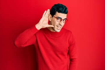 Handsome hispanic man wearing casual clothes and glasses smiling with hand over ear listening and hearing to rumor or gossip. deafness concept.