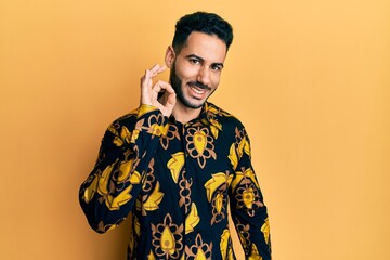 Young hispanic man wearing casual shirt smiling positive doing ok sign with hand and fingers. successful expression.
