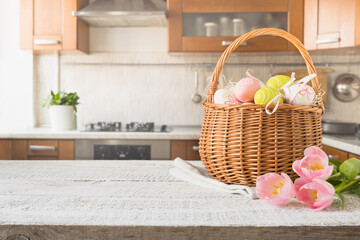 Easter wicker basket with painted eggs and tulips on kitchen white wooden tabletop. Spring...