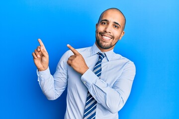 Hispanic adult man wearing business shirt and tie smiling and looking at the camera pointing with two hands and fingers to the side.