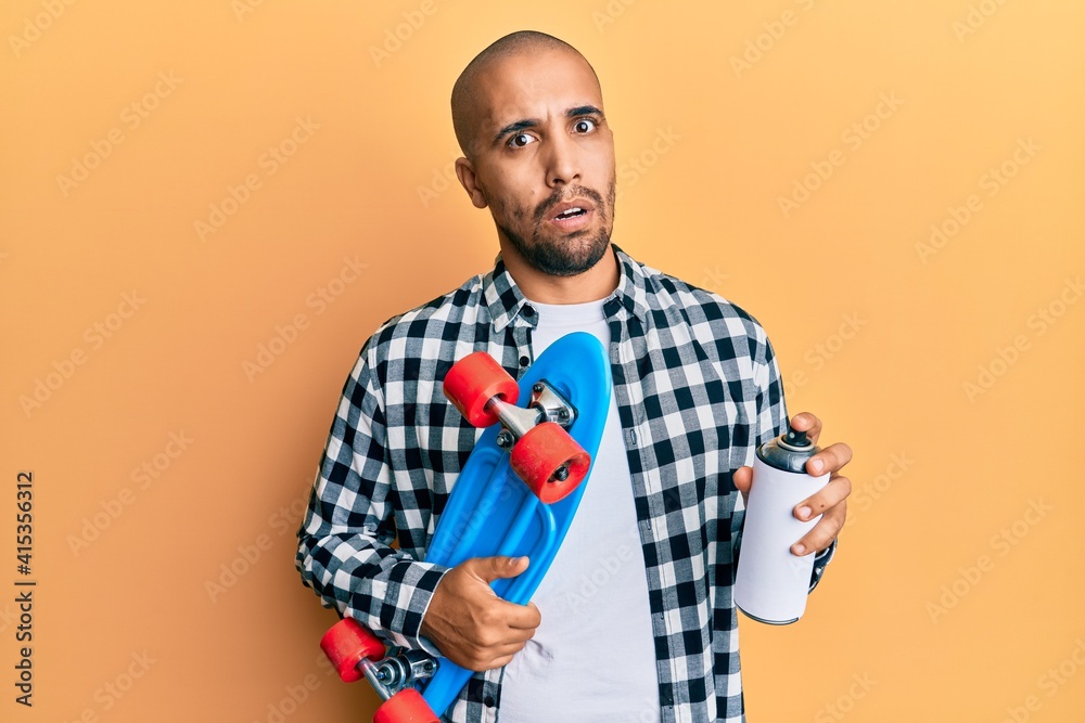 Sticker Hispanic adult skater man holding skate and graffiti spray in shock face, looking skeptical and sarcastic, surprised with open mouth