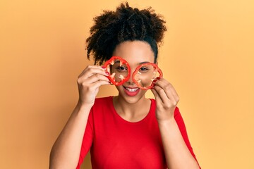 Young african american girl holding red pepper as a glasses smiling and laughing hard out loud because funny crazy joke.