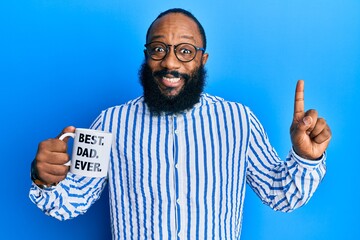 Young african american man drinking mug of coffe with best dad ever message smiling with an idea or question pointing finger with happy face, number one