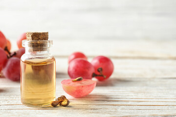 Organic red grapes, seeds and bottle of natural essential oil on white wooden table. Space for text