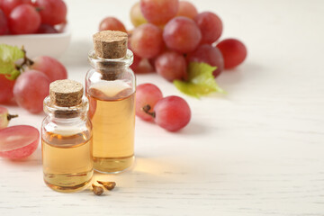 Organic red grapes, seeds and bottles of natural essential oil on white wooden table