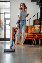 Happy woman with cordless vacuum easy cleaning floor at home in stylish interior design of living...