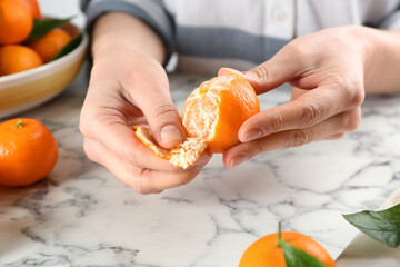 Woman peeling fresh ripe tangerine at white marble table, closeup