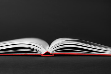 Open book with red cover on black background, closeup view