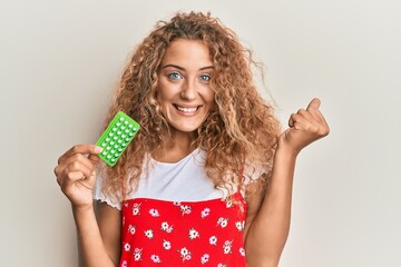 Beautiful caucasian teenager girl holding birth control pills screaming proud, celebrating victory and success very excited with raised arm