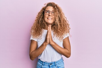 Beautiful caucasian teenager girl wearing white t-shirt over pink background begging and praying...
