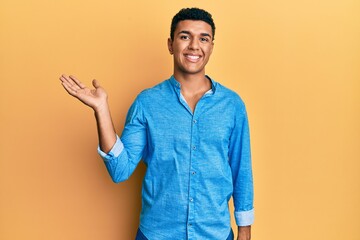 Young arab man wearing casual clothes smiling cheerful presenting and pointing with palm of hand looking at the camera.