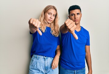 Young interracial couple wearing casual clothes looking unhappy and angry showing rejection and negative with thumbs down gesture. bad expression.