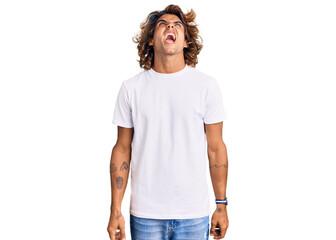 Fototapeta premium Young hispanic man wearing casual white tshirt angry and mad screaming frustrated and furious, shouting with anger. rage and aggressive concept.