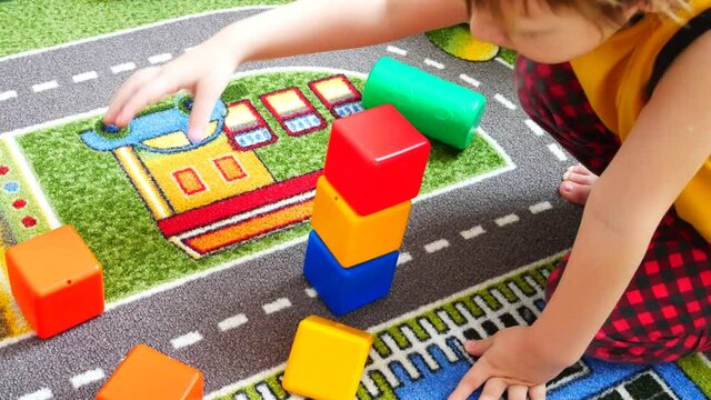 A little boy builds a tower using a few plastic cubes on a colorful carpet close-up