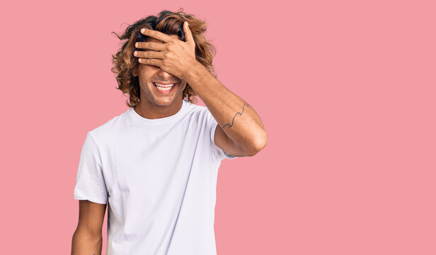 Young hispanic man wearing casual white tshirt smiling and laughing with hand on face covering eyes for surprise. blind concept.