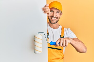 Young handsome man holding roller painter over white banner smiling with a happy and cool smile on...