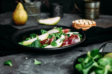 Parma, pear and spinach salad on black plate